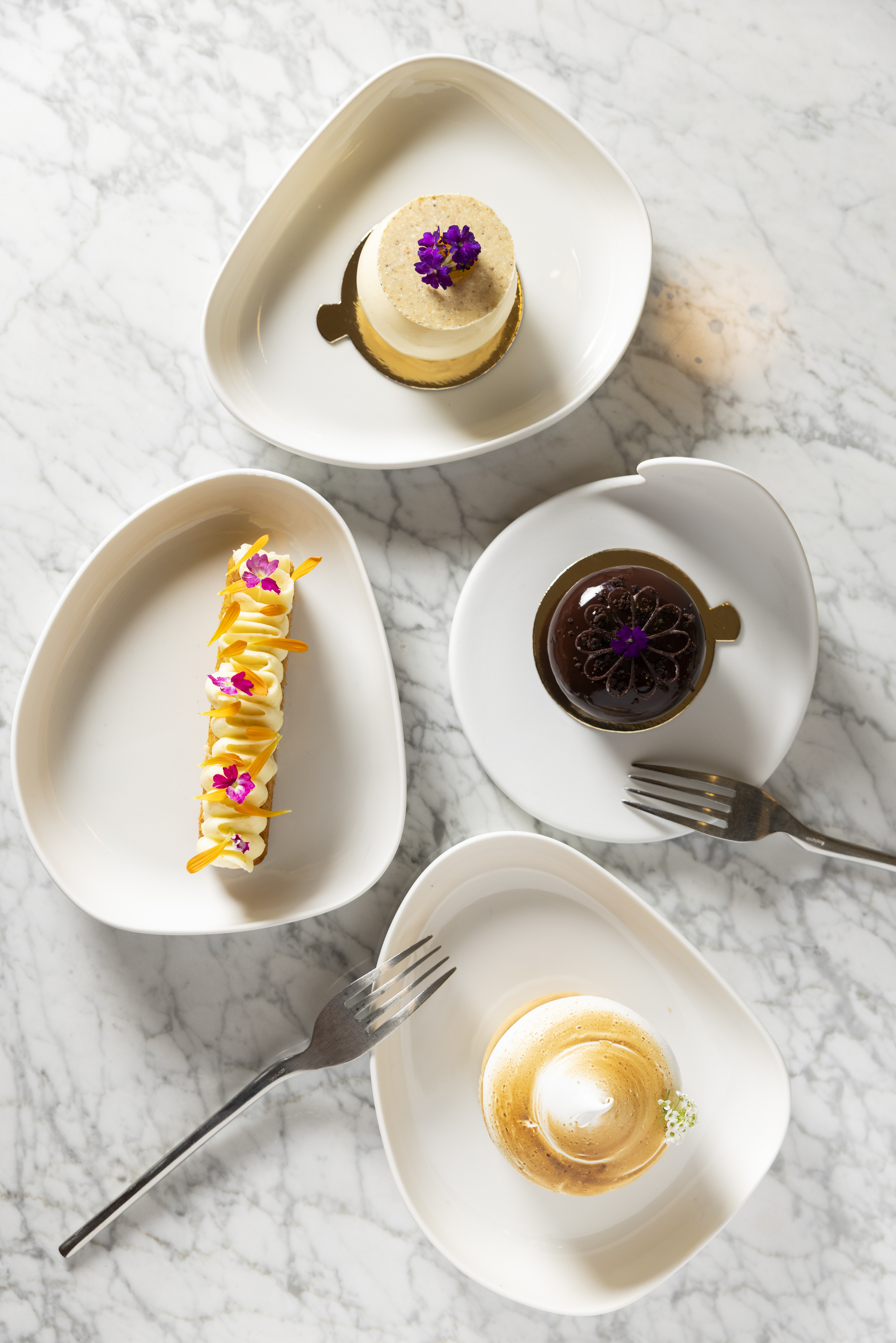 Cuatro pasteles artesanales en platos blancos sobre mármol